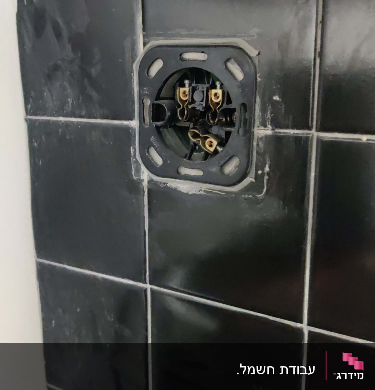 שקע חשמלי פתוח בקיר אריחים שחורים